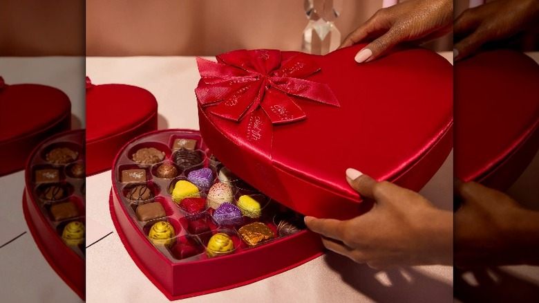 hands opening red heart-shaped box of chocolates