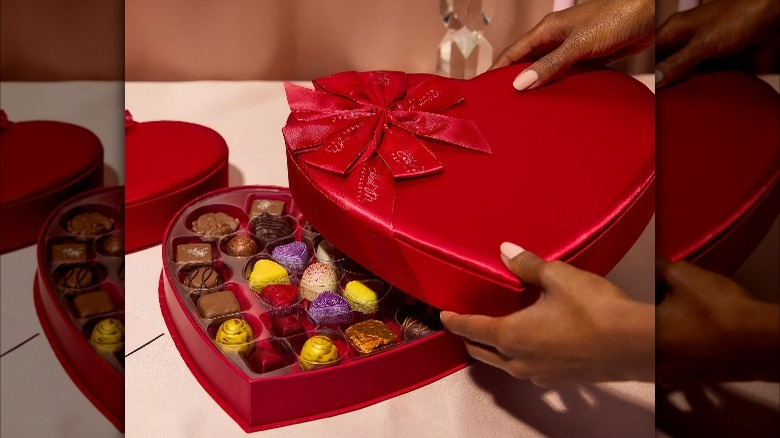 hands opening red heart-shaped box of chocolates