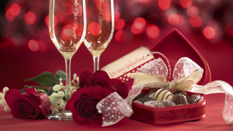 chocolates in a heart-shaped box with roses and some type of sparkling drink in flute-shaped glasses