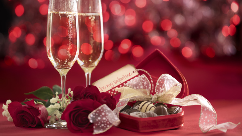 chocolates in a heart-shaped box with roses and some type of sparkling drink in flute-shaped glasses