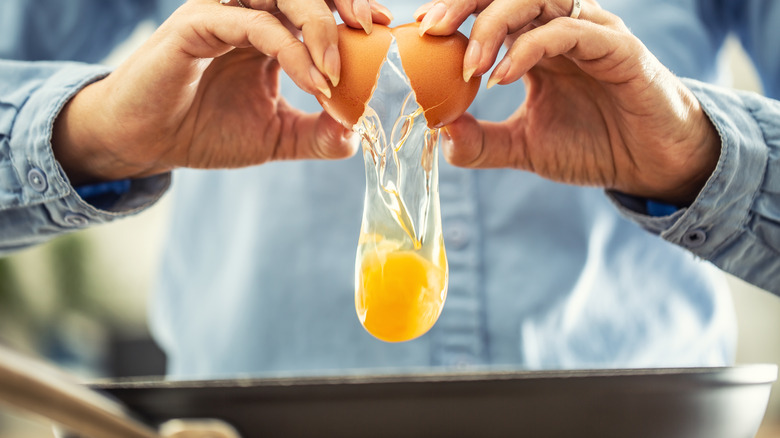 Hands cracking egg over pan