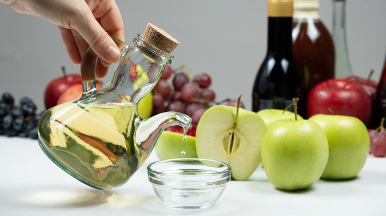 Handheld bottle of apple cider vinegar dripping into glass ramekin