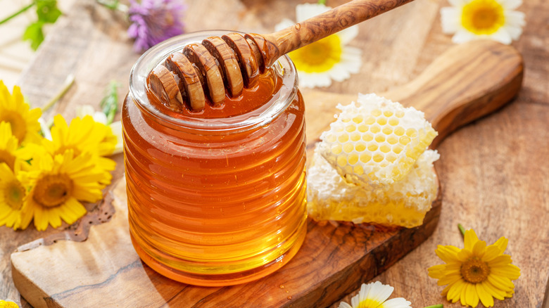 Honeycomb and honey jar by flowers