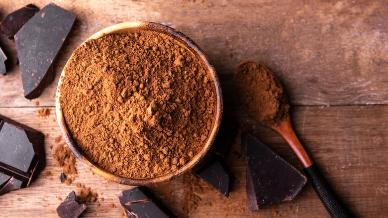 Bowl of cocoa powder by chocolate chunks and spoon