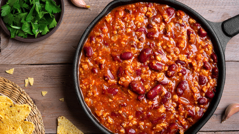 Cast-iron pan of chili by herbs and chips