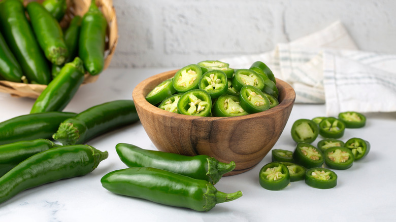 Wooden bowl of cut jalapeños by whole peppers