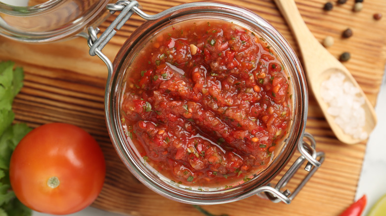 Salsa jar by fresh tomato on wooden countertop