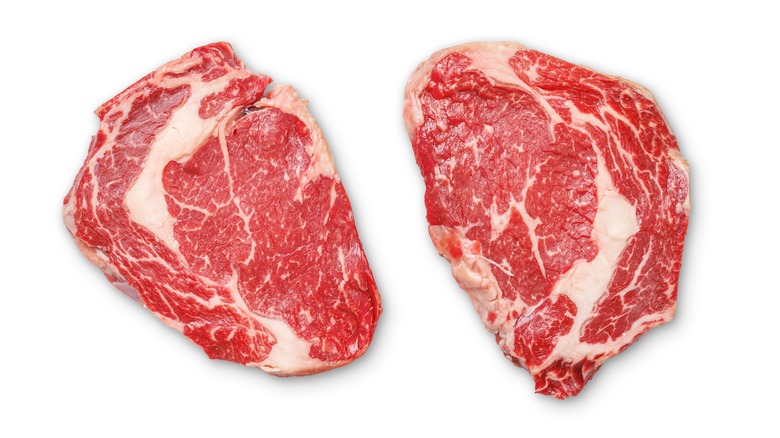 two raw ribeye steaks against a white background