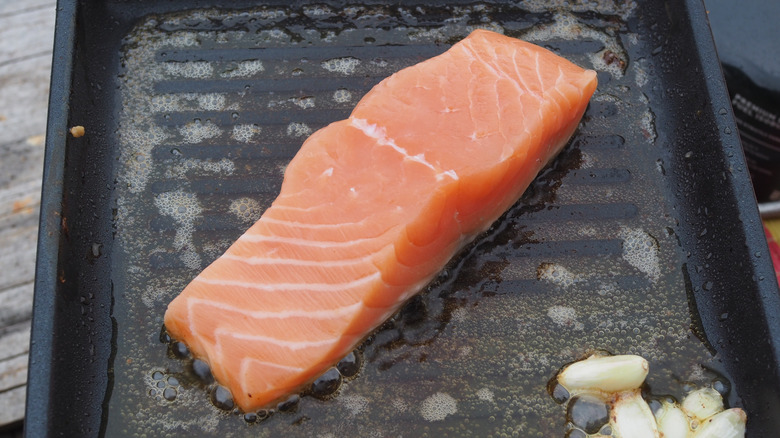 A raw salmon steak on a grill with garlic cloves and oil