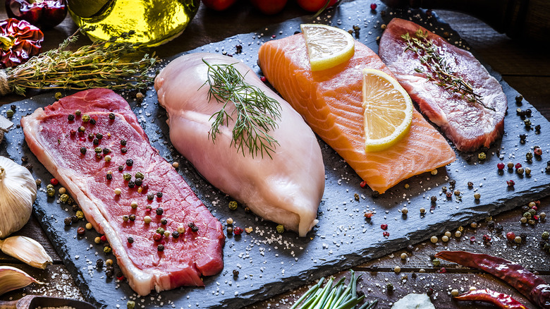 An assortment of raw meat on a stone platter decorated with herbs and spices