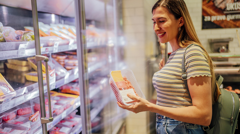 young woman shopping in the frozen meat section of a supermarket