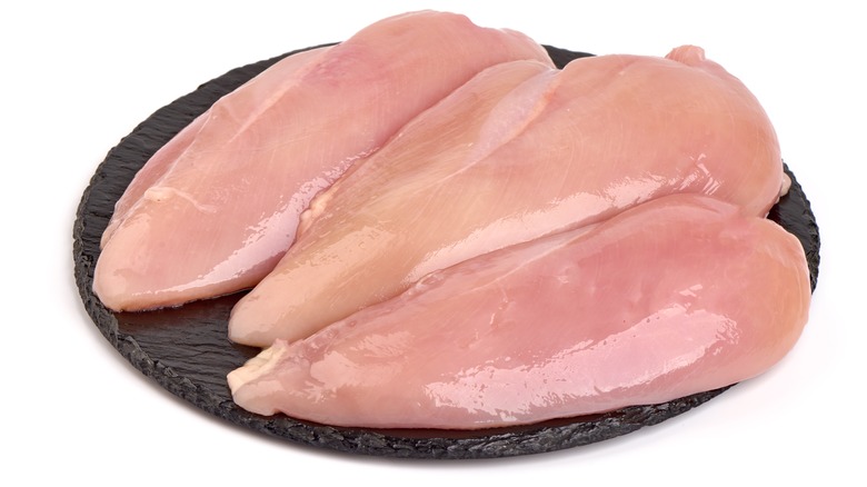 Three raw chicken breasts on a black slate plate