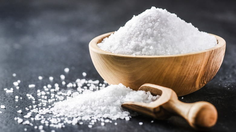 Natural, organic salt in a small bowl with a spoon of salt nearby and a pile of salt beneath the spoon