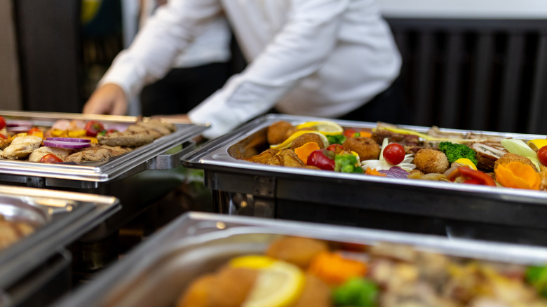 chafing dishes full of food with a server in the background