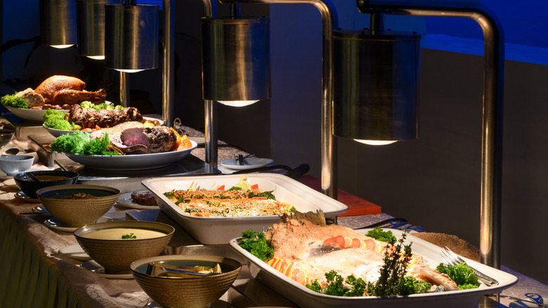 A row of entrees under lamps at a buffet