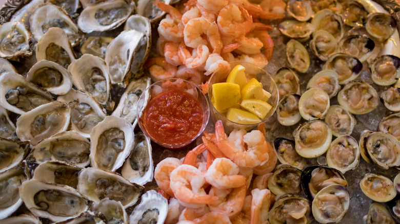 Oysters, shrimp, and clams with cocktail sauce and lemon wedges at a buffet.