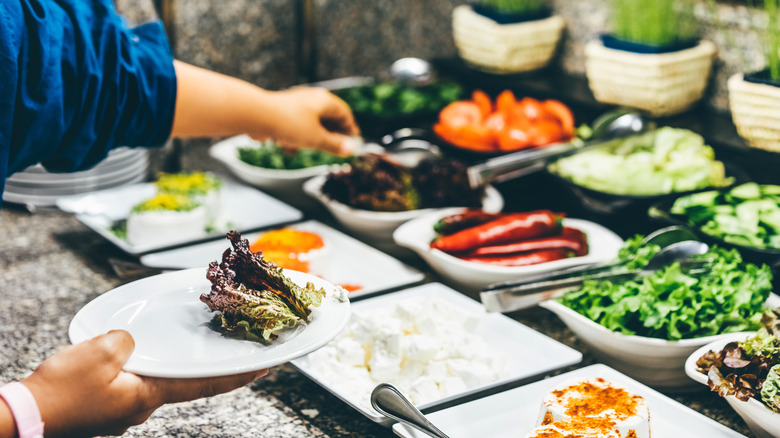 a person filling a plate from a salad bar