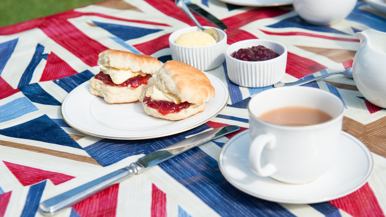 scones with cream and jam and a cup of milky tea on a Union Jack-patterned tablecloth