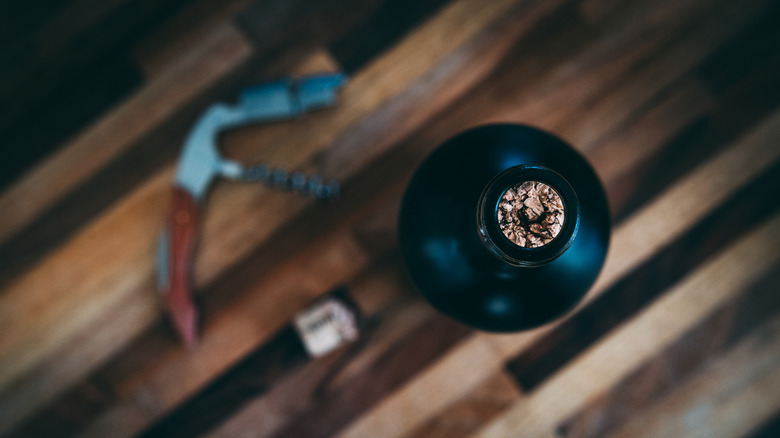 A wine opener and broken cork sit next to a wine bottle.