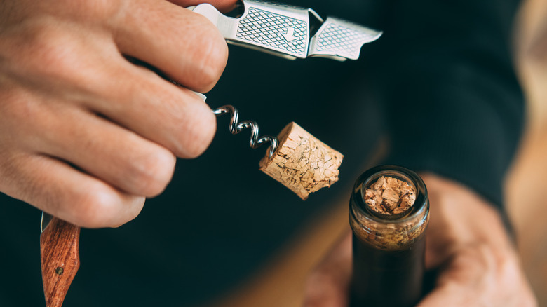 hand holding corkscrew pulling broken cork out of wine bottle