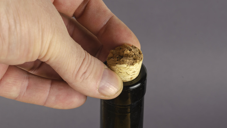 A hand grabbing the broken cork sticking out of a wine bottle