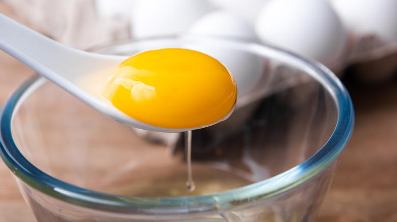 Egg yolk on spoon above glass bowl