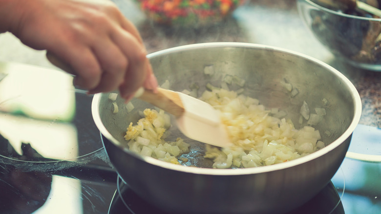 Woman stirs onions in pan