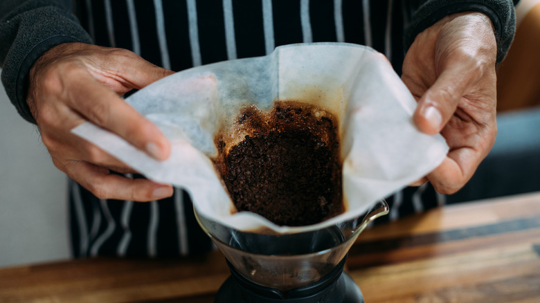 hands holding filter full of coffee grounds