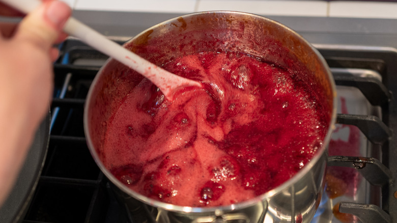 Close-up of person making red fruit jam on the stovetop