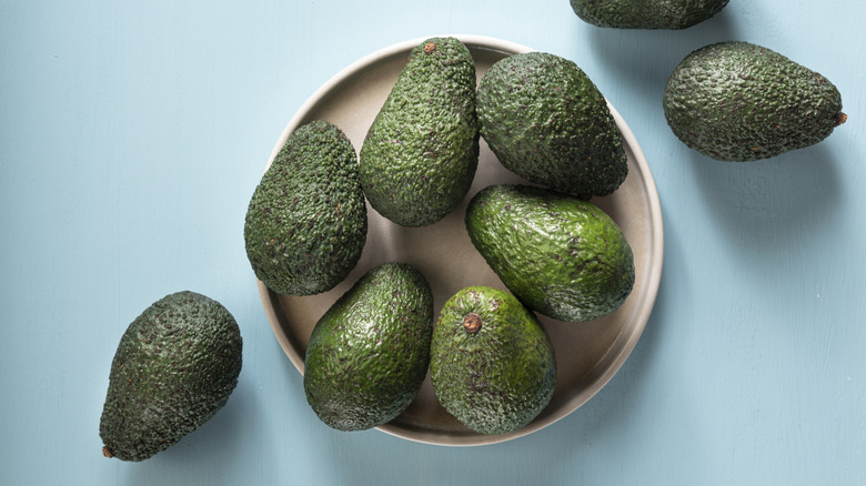 whole avocados on a beige plate and a blue surface