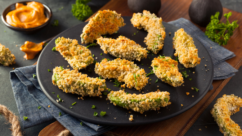 avocado fries on a black plate with a creamy orange-colored dip