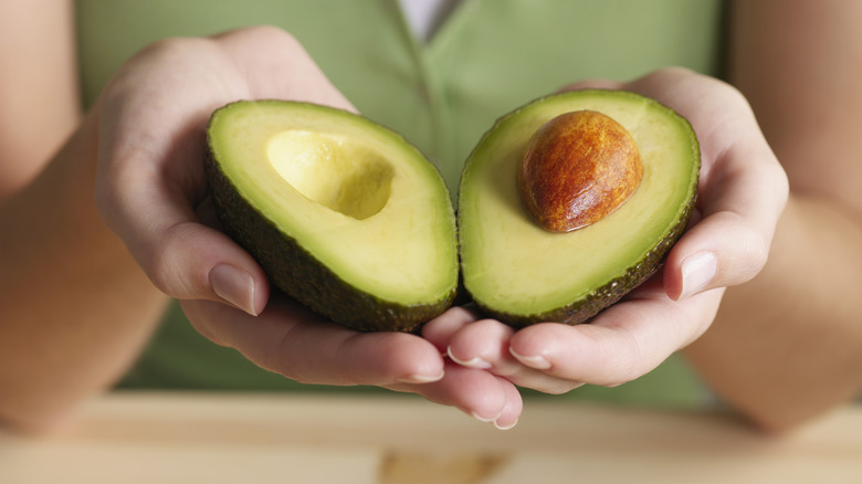 hands holding two avocado halves