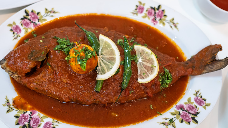 whole cooked fish topped with red sauce on a white plate with a pink floral pattern