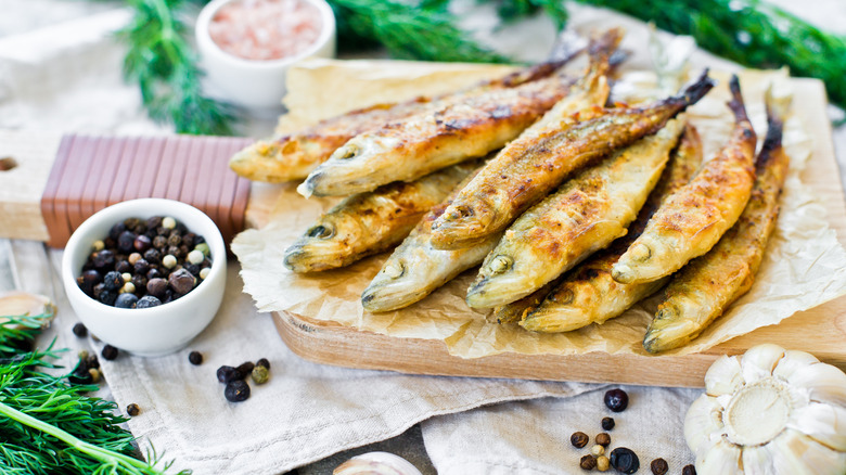 fried smelts on a wooden board next to a bowl of peppercorns