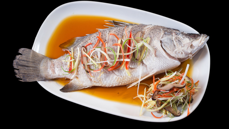 steamed striped bass in sauce on a white plate