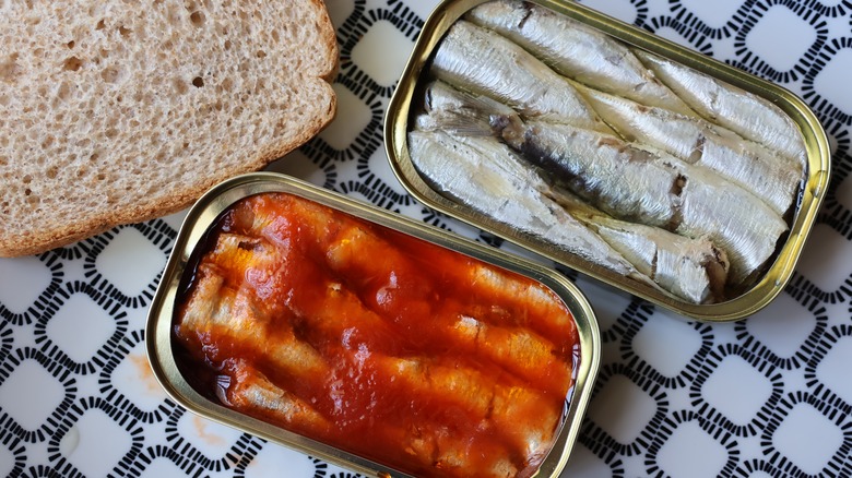 Open cans of sardines next to piece of bread