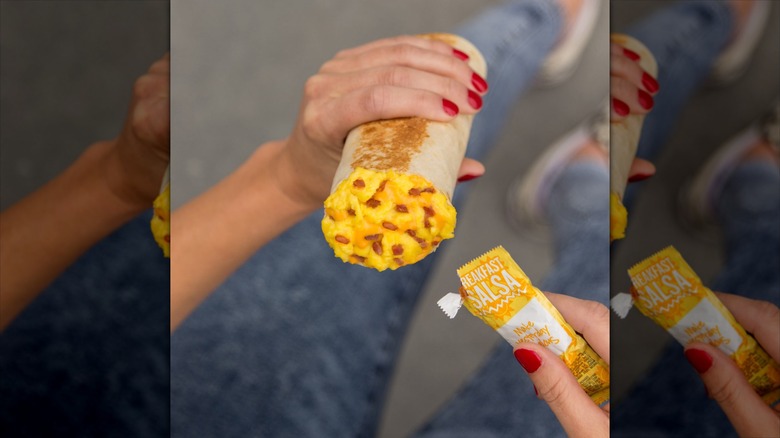 Person holding Taco Bell breakfast burrito and salsa packet