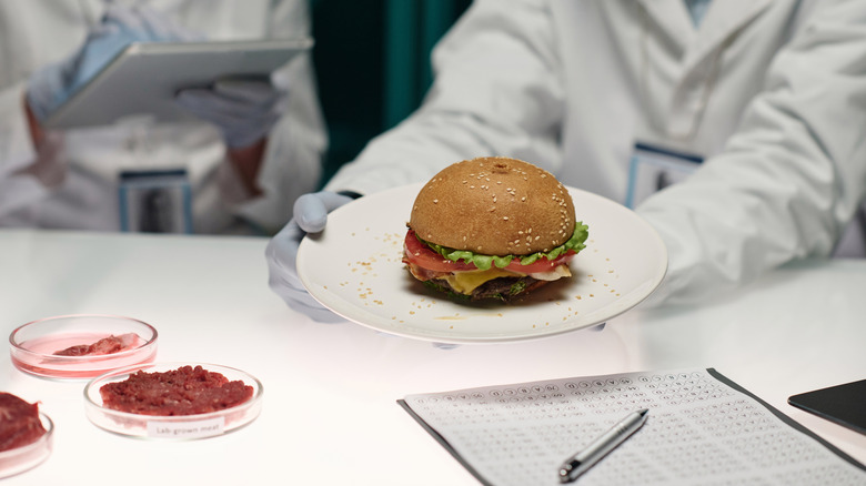 Scientist holds burger next to raw meat in petri dishes