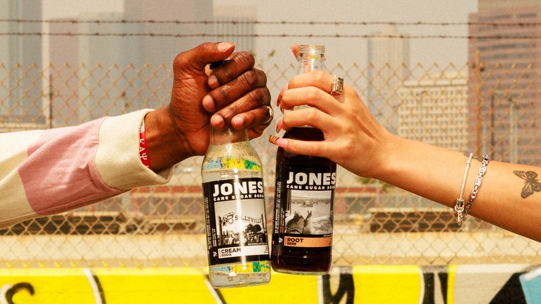 Hands holding Jones Soda in front of barbed wire