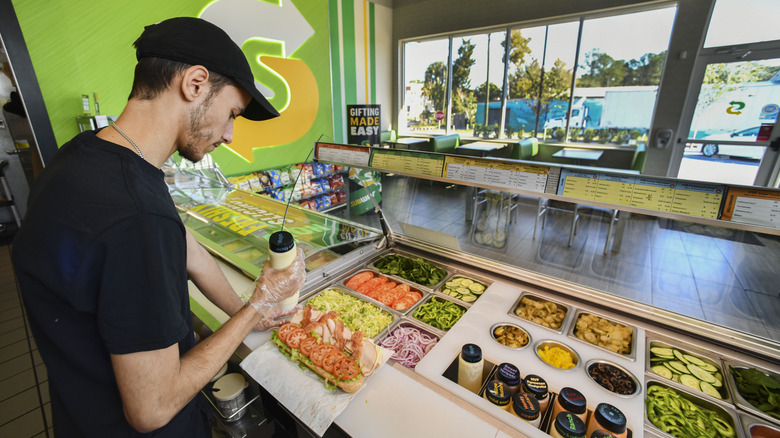 Subway sandwich artist spreading sauce on sub