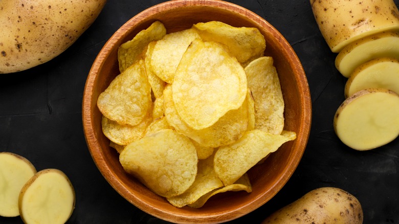 Potato chips in a bowl surrounded by raw sliced potatoes