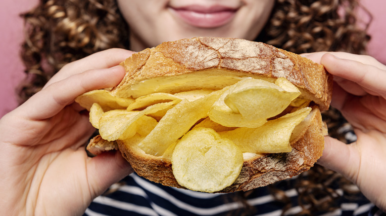 A woman holding a potato chip sandwich on white bread