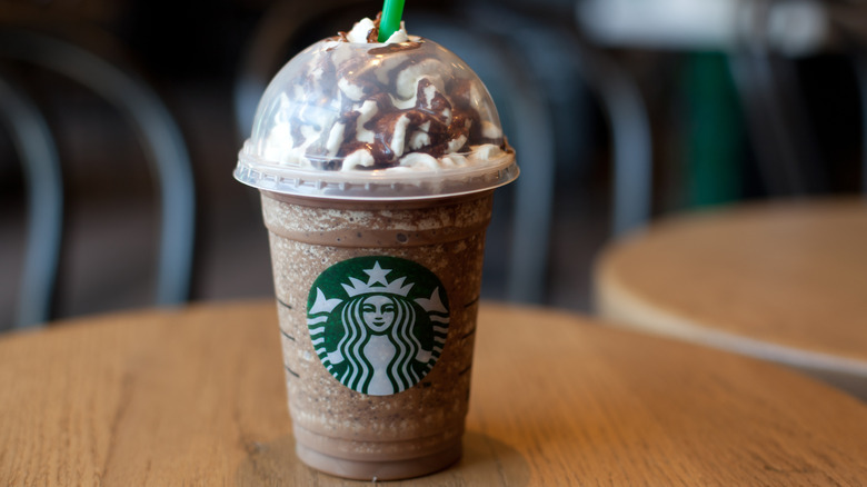 Starbucks mocha Frapuccino with whipped cream and chocolate drizzle and a green straw on a wooden table.