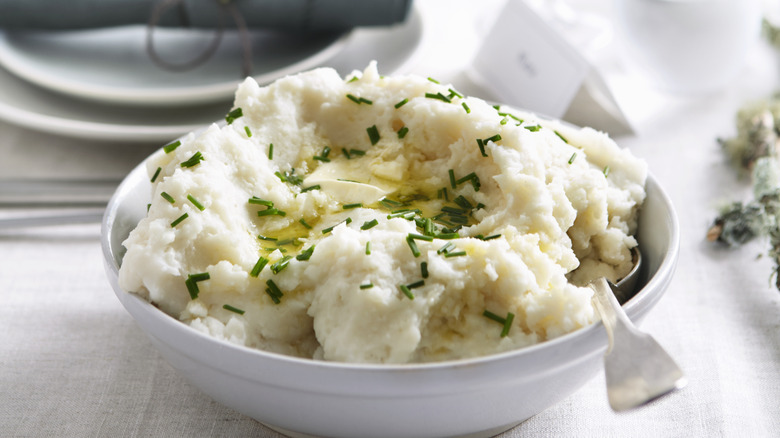 A bowl of mashed potatoes with melted butter and chopped chives.