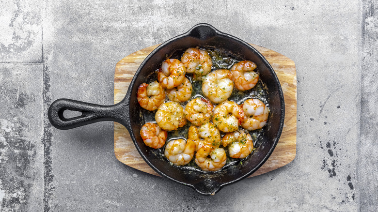 Cooked shrimp in a cast-iron skillet resting on a wooden cutting board