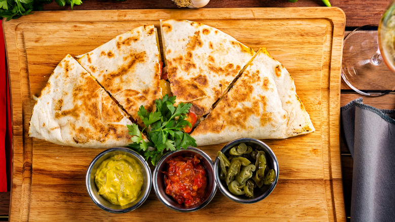 A quesadilla with sauces on a cutting board