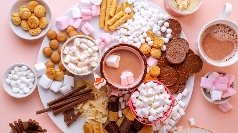 A board of dessert options with hot chocolate, cookies, caramels, marshmallows, and wafers.