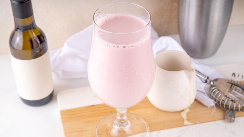 Pink beverage in a wine glass with bar tools