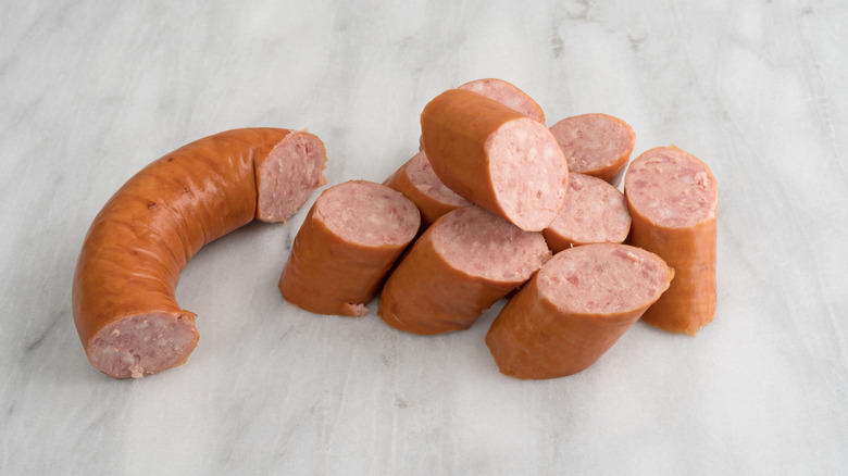 Sliced kielbasa next to large curved chunk on marble board