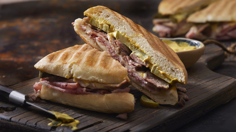 A traditional Cuban sandwich, sliced in half to show the ingredients inside, served on a wooden tray.